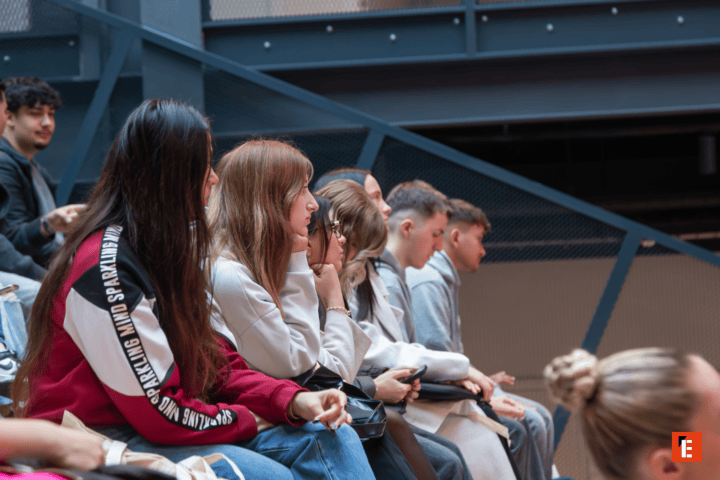 Spectateurs assis en rangée dans un espace industriel, étudiants attentifs en profil.