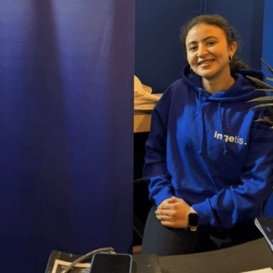 Stand dinformation bleu avec personne souriante, brochures, plante et smartphone sur table.