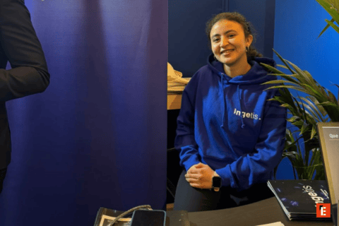 Stand dinformation bleu avec personne souriante, brochures, plante et smartphone sur table.