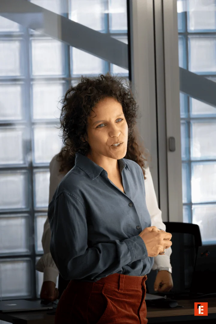 Deux hommes en réunion avec ordinateurs Apple dans espace de travail moderne près dascenseurs.