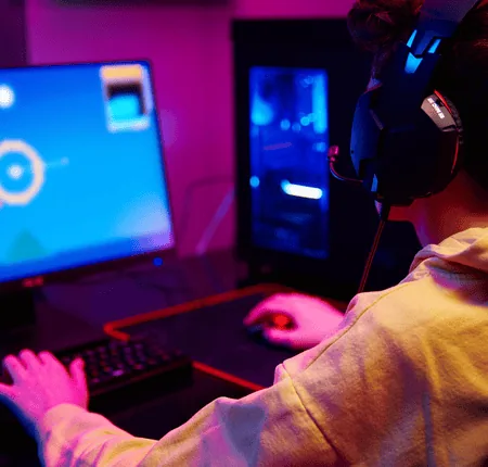 Configuration gaming nocturne : joueur au casque devant écran, PC RGB bleu, clavier mécanique et souris.