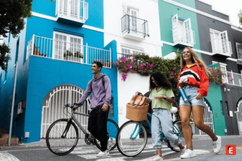 Amis avec vélos traversant un passage piéton devant maisons colorées en ville.