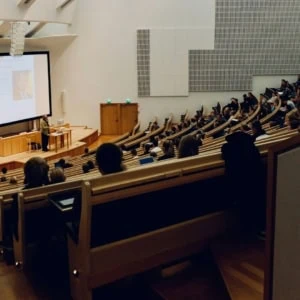 Amphithéâtre moderne avec conférencier, écran projeté et étudiants éparpillés.