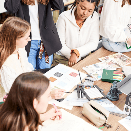 Équipe en atelier de dessin collaboratif, croquis, crayons, feutres et échantillons sur table.
