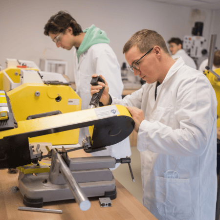 Atelier machines-outils avec scies, techniciens en blouse blanche et équipements de sécurité.