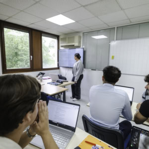 Atelier en petite salle de formation avec formateur, participants, écran et ordinateurs portables.