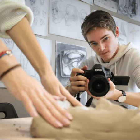 Photographe en atelier capturant des mains modelant largile avec un Canon.