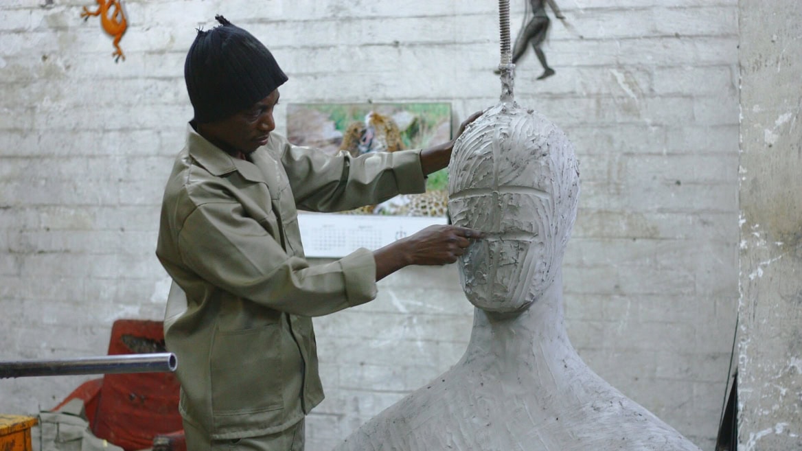 Sculpteur en atelier modelant un buste en argile, mains travaillant le visage.