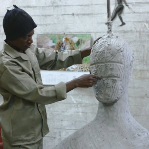 Sculpteur en atelier modelant un buste en argile, mains travaillant le visage.