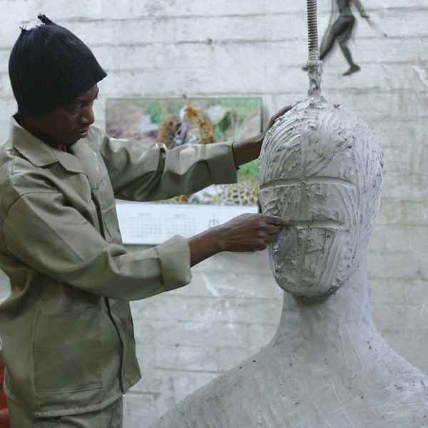 Sculpteur en atelier modelant un buste en argile, mains travaillant le visage.