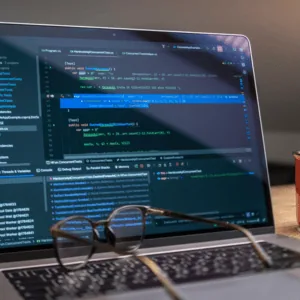 Bureau avec ordinateur portable affichant du code, lunettes sur clavier et mug «MAKE it HAPPEN».