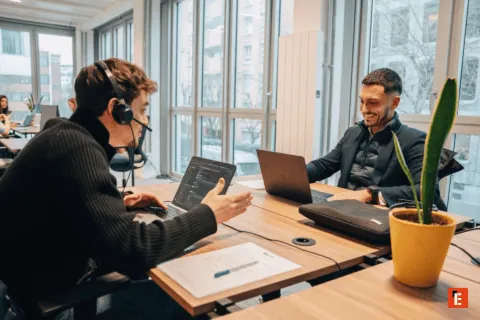 Bureau coworking lumineux avec collègues en collaboration, ordinateurs et grandes fenêtres.
