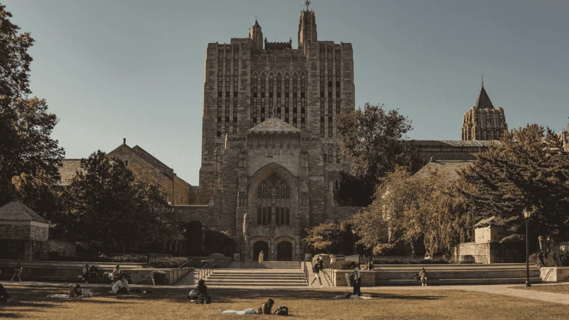 Entrée monumentale gothique du campus avec pelouse, escaliers et étudiants au soleil.