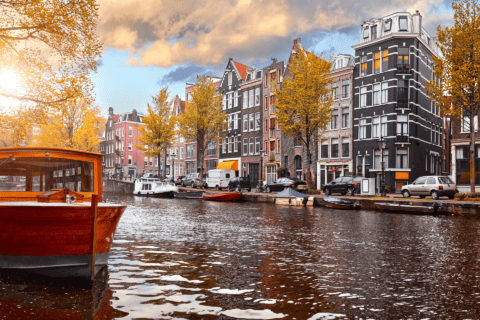 Bateau en bois sur canal automnal, quai et maisons de ville aux reflets dorés.