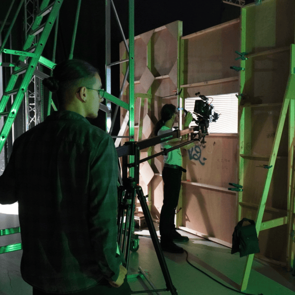 Coulisses de tournage : opérateur caméra sur grue, plateau avec échelle et éclairage vert.