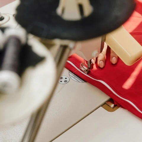 Machine à coudre cousant passepoil blanc sur tissu rouge.