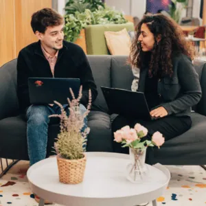 Espace coworking lounge moderne : deux personnes collaborent avec ordinateurs portables sur canapé.