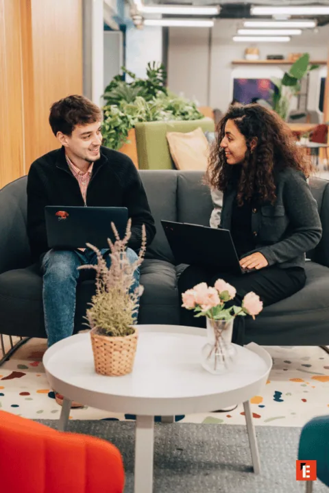 Espace coworking lounge moderne : deux personnes collaborent avec ordinateurs portables sur canapé.