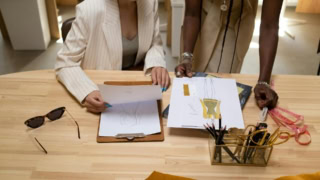 Croquis de mode en atelier : créateurs collaborent autour de dessins, tissus et outils.