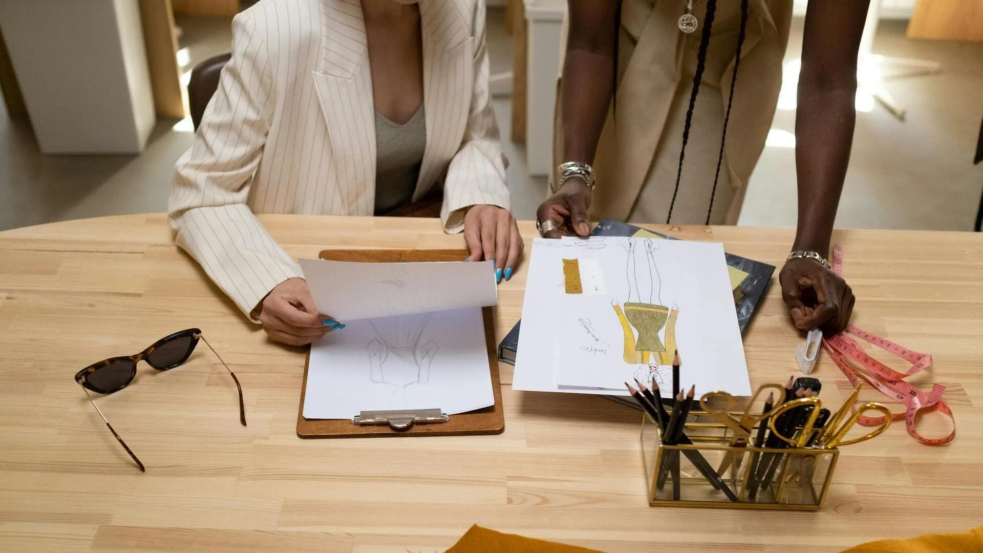 Croquis de mode en atelier : créateurs collaborent autour de dessins, tissus et outils.