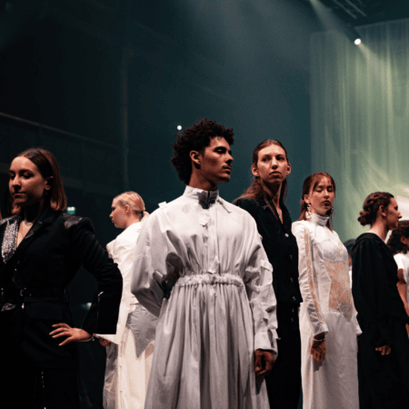 Défilé de mode minimaliste en noir et blanc, mannequins alignés sous projecteur.