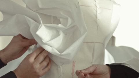Drapage sur mannequin de toile, couture main, mains ajustant tissu blanc et épingles.