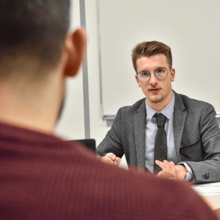 Entretien professionnel en bureau : homme en costume discutant face à face, ordinateur visible.