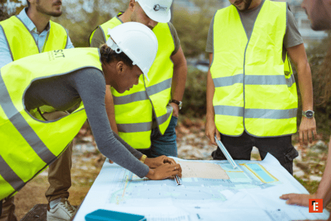 Équipe de chantier examinant des plans sur table, gilets haute visibilité et casques.