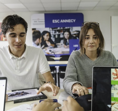 Étudiants ESC Annecy en travail de groupe collaboratif avec ordinateurs dans une salle détude moderne.