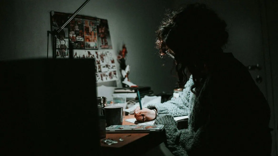 Personne dessinant au bureau la nuit, lampe focalisée, ambiance créative et intime.