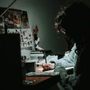 Personne dessinant au bureau la nuit, lampe focalisée, ambiance créative et intime.