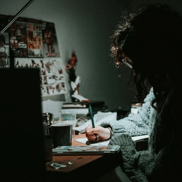 Personne dessinant au bureau la nuit, lampe focalisée, ambiance créative et intime.