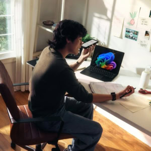 Étudiant au bureau lumineux travaillant avec téléphone, ordinateur portable, notes et plante verte.
