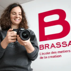 Étudiante en photographie manipulant un appareil photo Canon devant logo BRASSART, école de création.