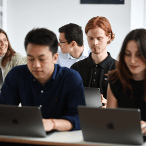 Étudiants en classe travaillant sur ordinateurs portables MacBook lors dun atelier collaboratif.