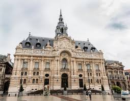Façade monumentale dun bâtiment historique en pierre, toiture mansardée et place humide.
