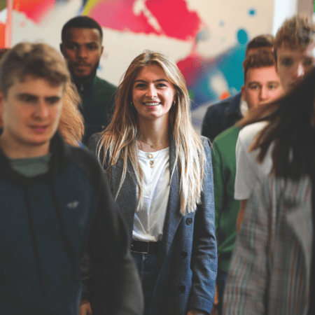 Femme souriante blonde en blazer dans un couloir urbain animé, portrait mode.