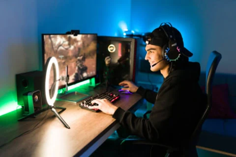 Gamer streaming souriant avec smartphone, ring light et PC gaming.