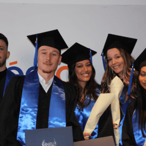 Cinq diplômés en toges, stoles bleues, tenant diplômes et bouquets, remise de diplômes.