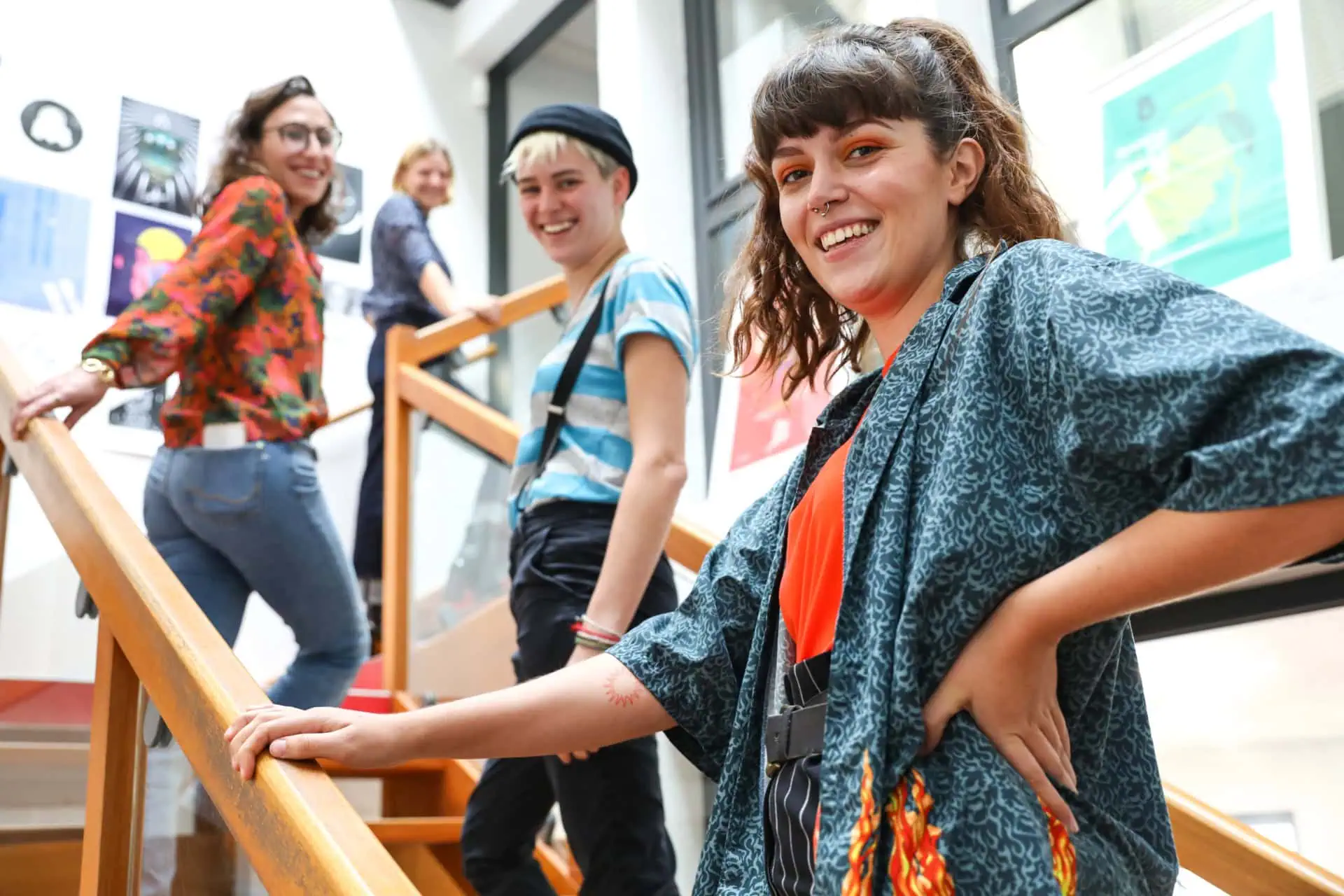 Groupe souriant sur escalier lumineux en studio créatif, portrait informel et tenues colorées.