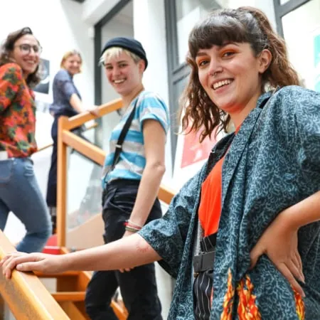 Groupe souriant sur escalier lumineux en studio créatif, portrait informel et tenues colorées.
