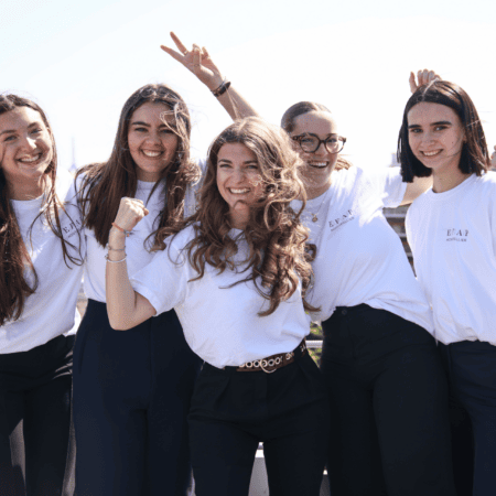 Groupe de jeunes femmes souriantes en t-shirts blancs sur toit-terrasse ensoleillé.