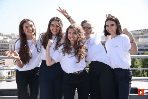 Groupe de jeunes femmes souriantes en t-shirts blancs sur toit-terrasse ensoleillé.