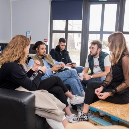 Groupe de jeunes adultes en lounge urbain discutant autour dun canapé et dune table basse.