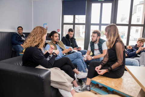 Groupe de jeunes adultes en lounge urbain discutant autour dun canapé et dune table basse.