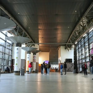 Hall public moderne lumineux avec colonnes, larges baies vitrées et passants.