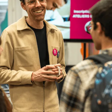 Homme souriant avec tasse de café, lunettes et veste beige lors dun événement convivial.