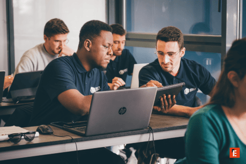 Hommes en formation professionnelle collaborant sur ordinateurs portables et tablettes en salle de classe.