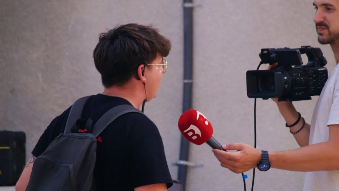 Interview de rue : journaliste tend un micro rouge vers une personne filmée par caméra.