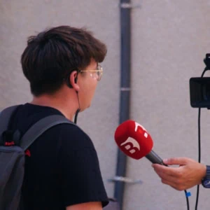Interview de rue : journaliste tend un micro rouge vers une personne filmée par caméra.